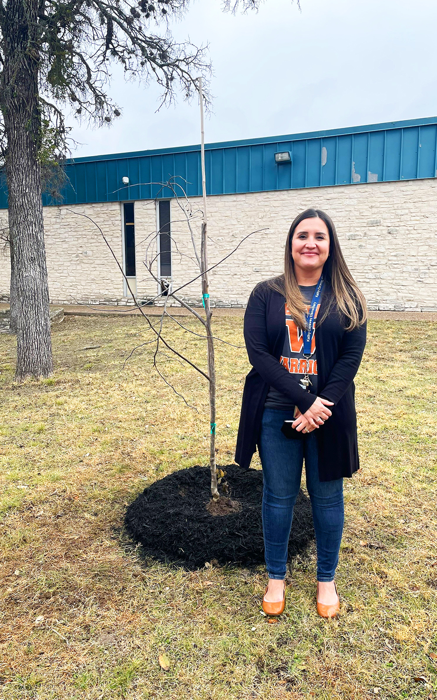 Principal Larissa Ortiz stands next to a young red bud tree on the Caraway Elementary school grounds.